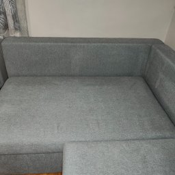 Daniel Stec - Szary narożnik z tkaniny, widok z góry, zarysowany kąt. Minimalistyczny design, jasne tło, widoczny fragment grzejnika i zasłony w tle.