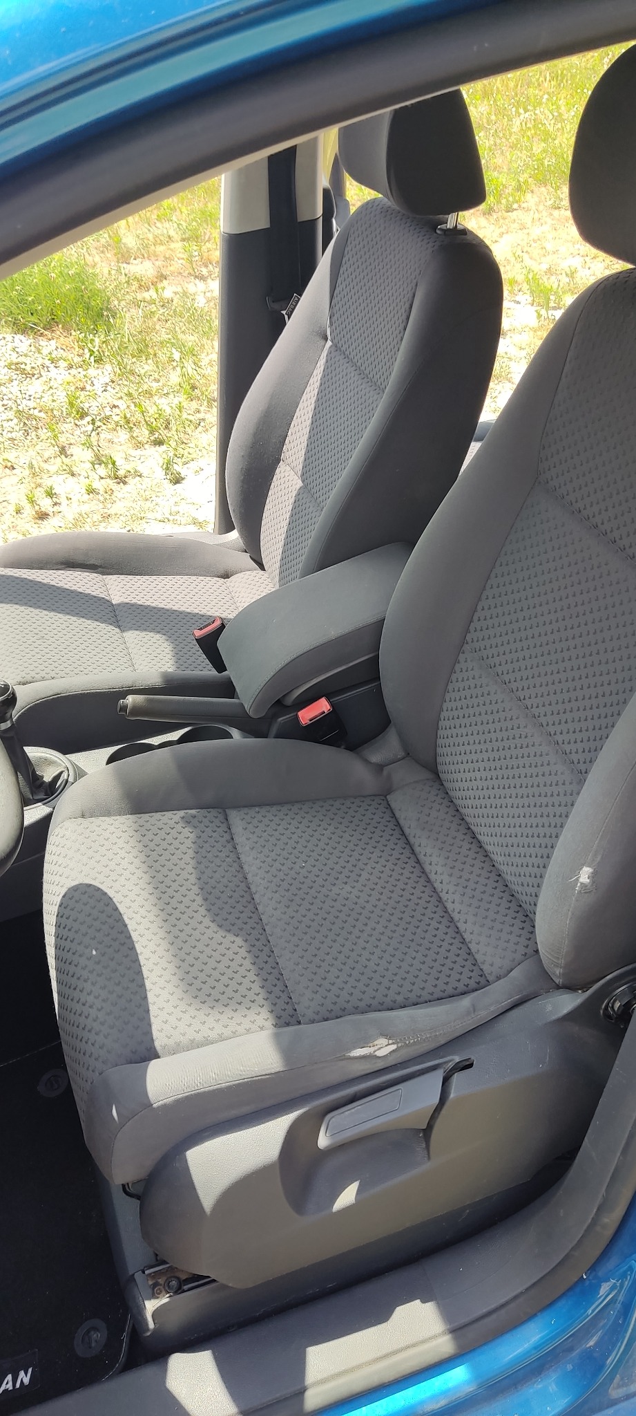 Wnętrze samochodu z szarą tapicerką foteli. Widoczne plamy i zabrudzenia na siedzeniach, zwłaszcza na fotelu kierowcy. Fotel pasażera w lepszym stanie.