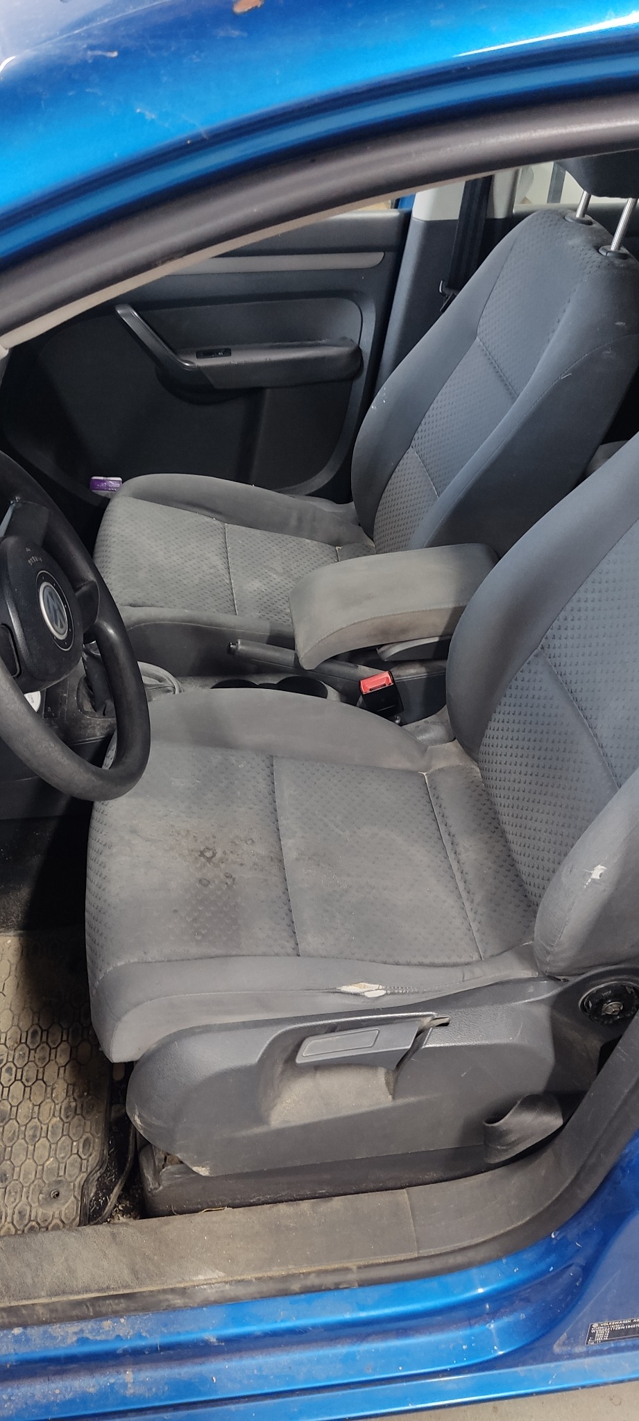 Wnętrze niebieskiego auta z widocznymi, mocno zabrudzonymi siedzeniami z szarej tapicerki. Widoczne plamy i uszkodzenia na fotelu kierowcy.