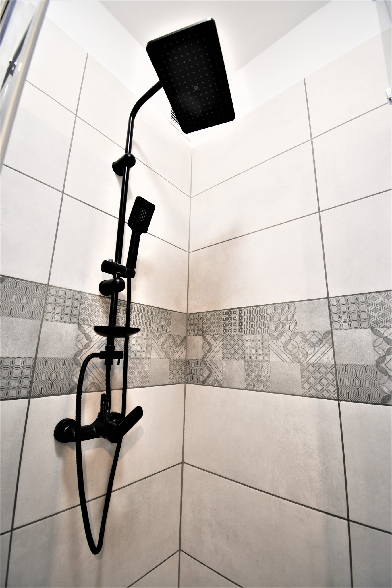Nowoczesna kabina prysznicowa z czarną armaturą i białymi płytkami z szarym dekoracyjnym pasem.
