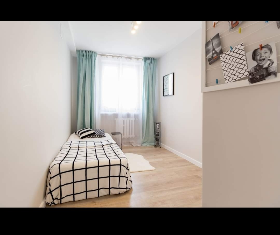 Jasny pokój z pojedynczym łóżkiem w czarno-białą kratę, turkusowymi zasłonami i dekoracyjną galerią zdjęć na sznurku z klamerkami.