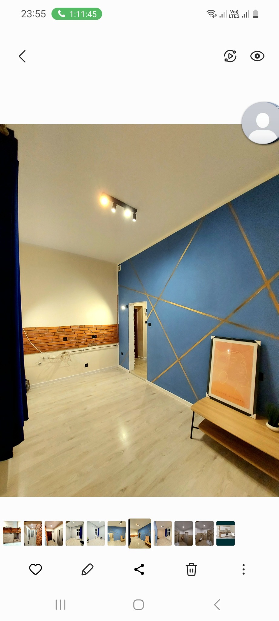 Pokój po odświeżeniu: ściana pomalowana na niebiesko z geometrycznymi złotymi wzorami, jasna podłoga, fragment ściany z cegieł, czarna lampa sufitowa i plakat na drewnianej konsoli.