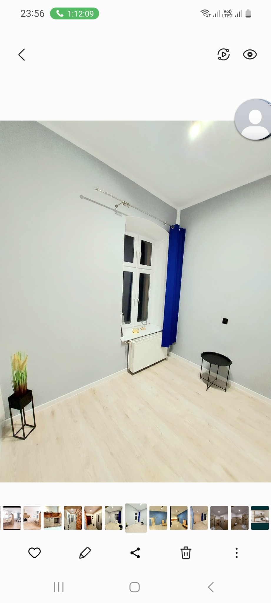 Pokój po odświeżeniu: szare ściany, jasna podłoga imitująca drewno, białe okno z niebieską zasłoną, czarny stolik i dekoracyjna roślina w czarnej donicy.