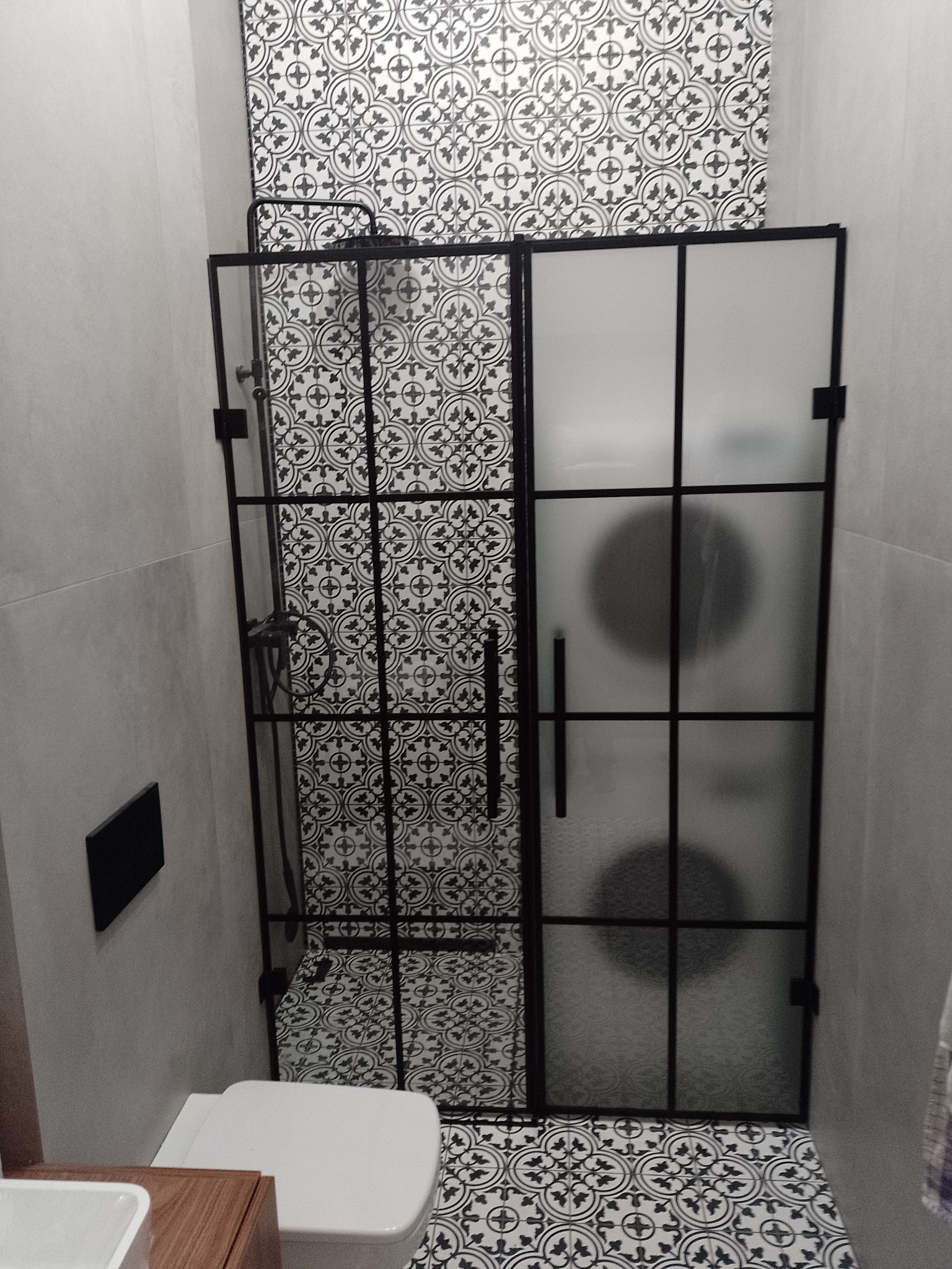 Kabina prysznicowa z czarnymi szprosami i częściowo matowym szkłem, dopasowana do wzoru płytek w łazience.