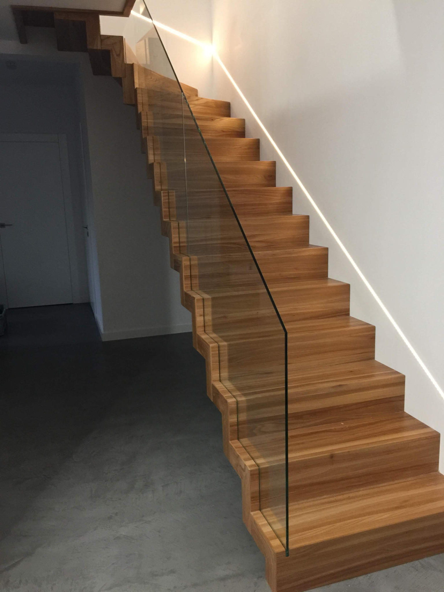 Schody drewniane z balustradą ze szkła, oświetlenie LED wzdłuż ściany, widok z dołu.