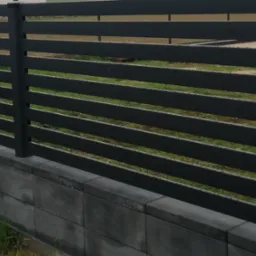 Nowoczesne, poziome ogrodzenie z szarych, metalowych paneli, osadzone na niskim murku z betonowych bloczków, z widoczną paletą w tle.