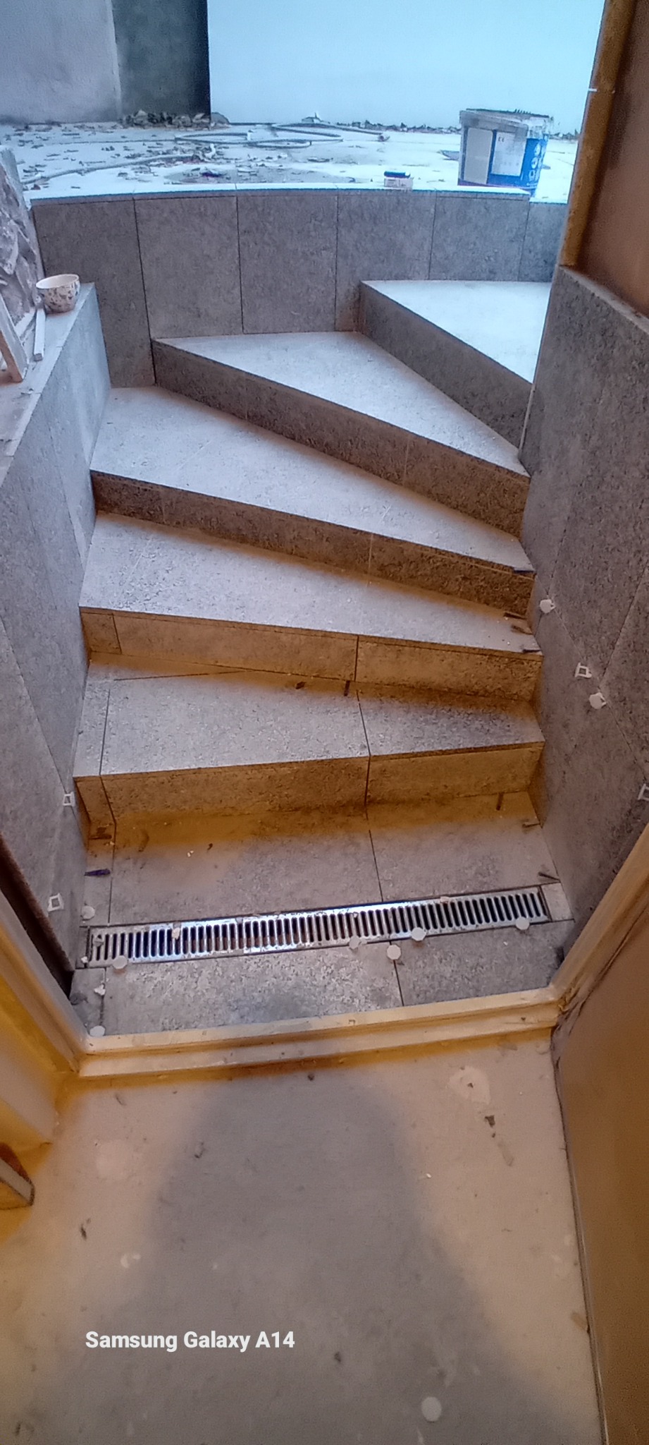 Schody wyłożone szarymi płytkami w trakcie montażu, widoczne krzyżyki dystansowe i odpływ liniowy.