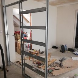 RAFEXAN RAFAŁ HELIASZ - Montaż metalowej konstrukcji ścianki działowej w trakcie remontu w Krakowie, widoczne narzędzia i materiały budowlane, surowy stan wykończenia wnętrza.