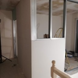 RAFEXAN RAFAŁ HELIASZ - Montaż ścianki działowej z płyt gipsowo-kartonowych na metalowym stelażu, widoczna drabina w tle, etap prac wykończeniowych w pomieszczeniu.