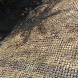 Siatka wzmacniająca skarpę z piasku, widok z góry pod kątem. Element stabilizacji gruntu na zboczu, przygotowany do dalszych prac ogrodniczych.