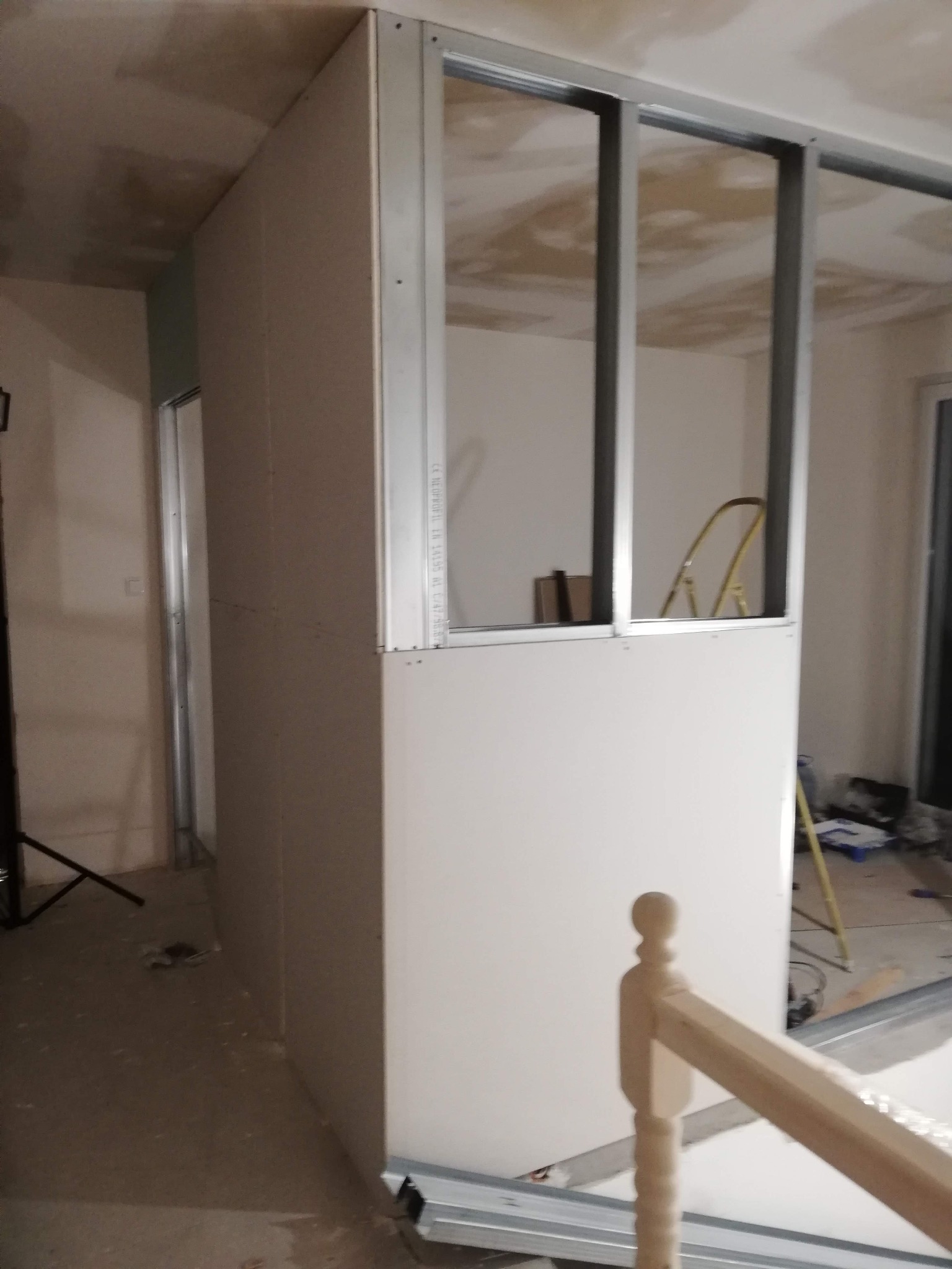 Montaż ścianki działowej z płyt gipsowo-kartonowych na metalowym stelażu, widoczna drabina w tle, etap prac wykończeniowych w pomieszczeniu.