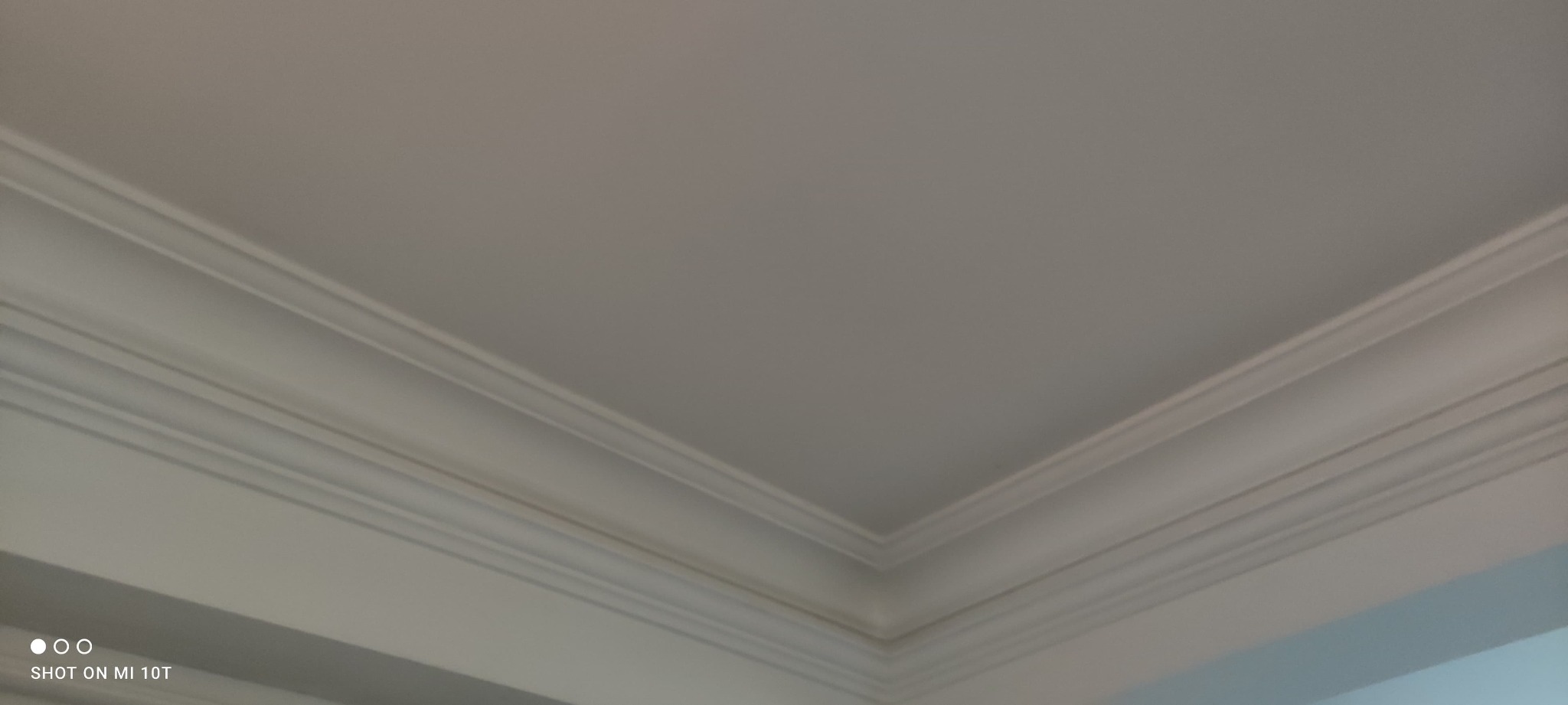 Biały sufit z dekoracyjnymi listwami przypodłogowymi, widok z dołu w rogu pomieszczenia.