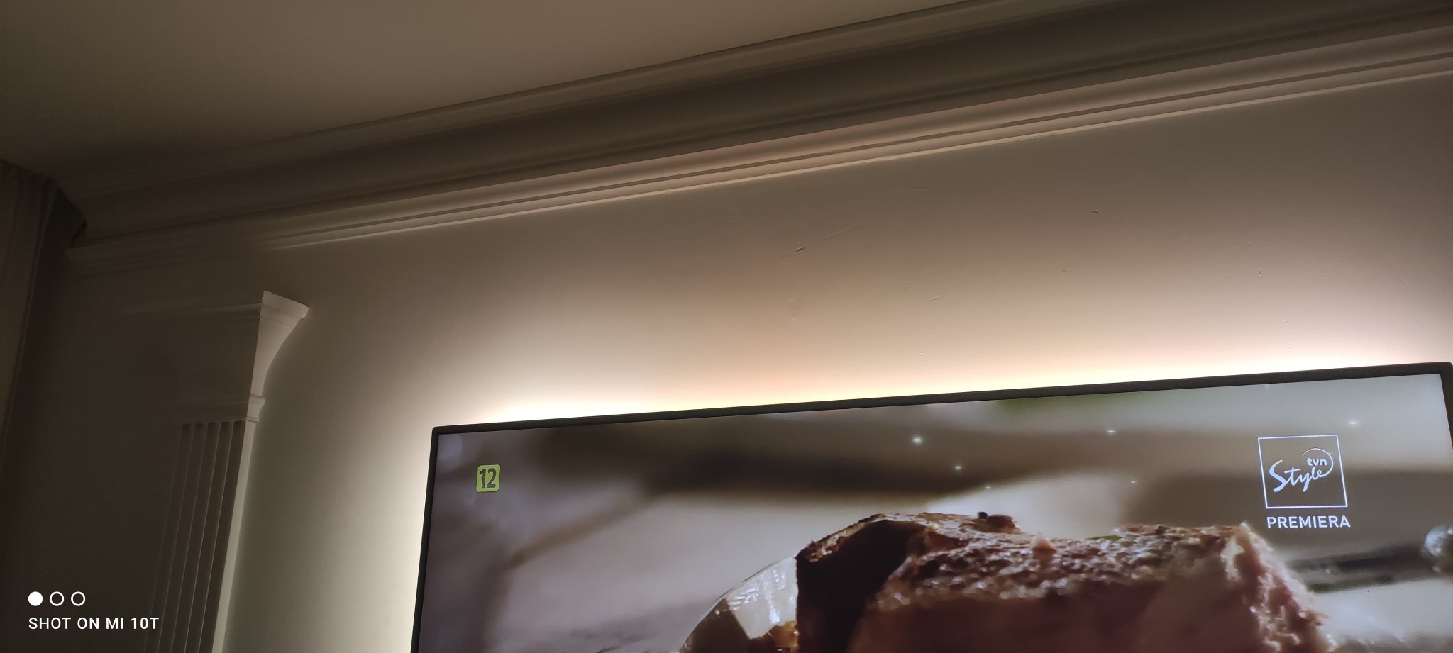 Ściana z dekoracyjną listwą sufitową i podświetleniem LED, widoczny fragment telewizora z logiem TVN Style.