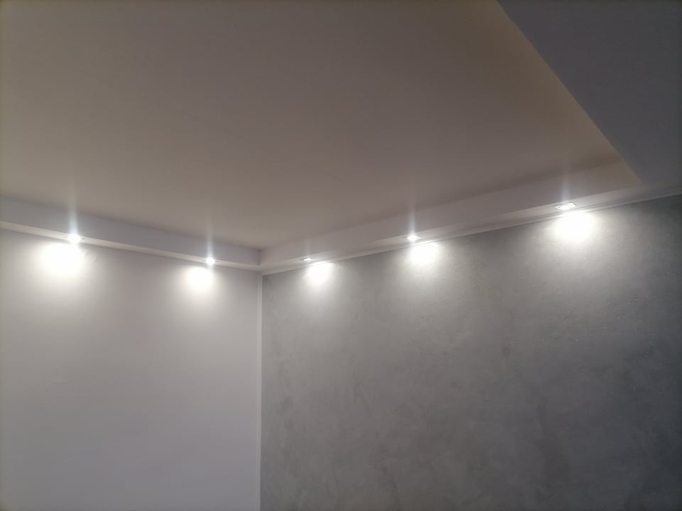 Nowoczesny sufit podwieszany z oświetleniem punktowym LED, ściana z dekoracyjną szarą fakturą, widok z dołu.