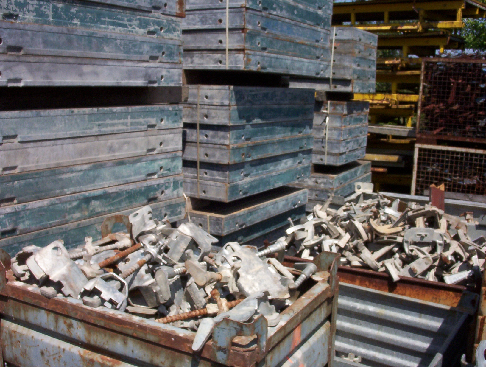 Stosy metalowych szalunków budowlanych i skrzynie z łącznikami na placu składowym.