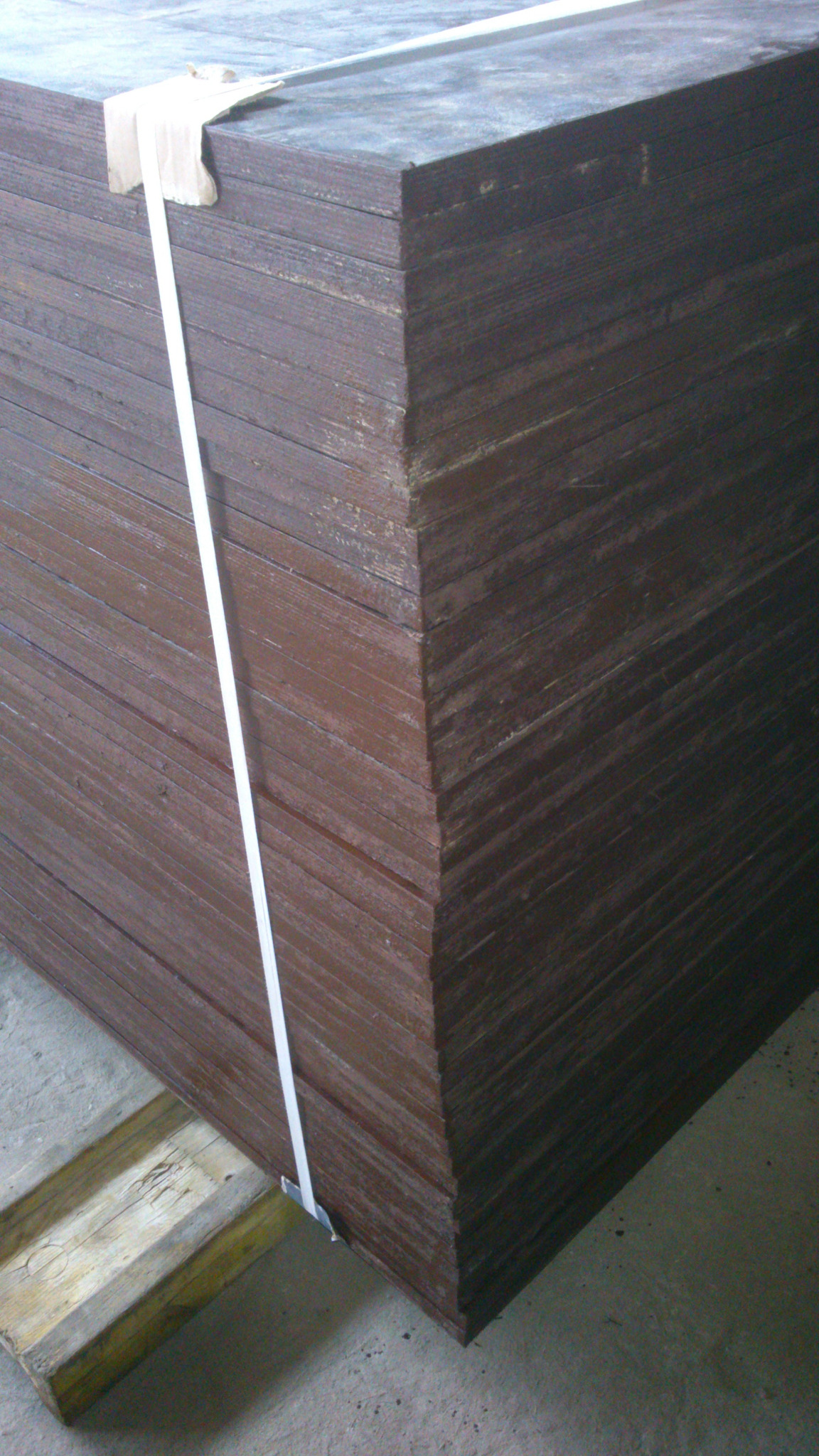 Stos brązowych, lakierowanych płyt szalunkowych na drewnianej palecie, zabezpieczonych białą taśmą.