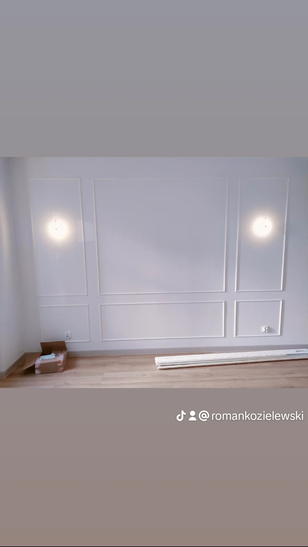 Ściana z zamontowanymi białymi listwami dekoracyjnymi w stylu klasycznym, podłoga z paneli, karton i listwy przypodłogowe leżące na podłodze.
