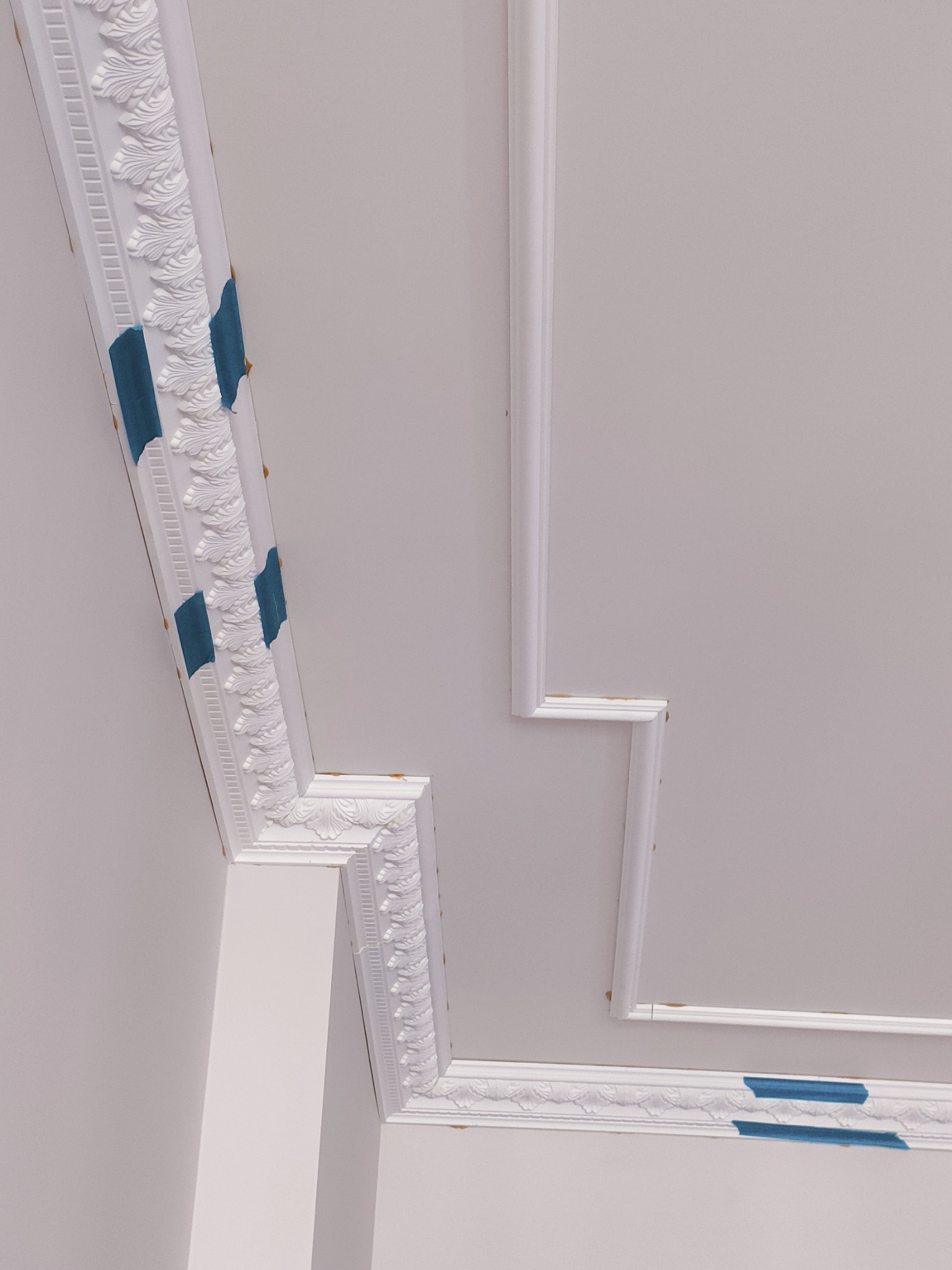 Dekoracyjny, biały sztukateryjny sufit z maskującą niebieską taśmą malarską, zbliżenie na narożnik i fragment ściany.