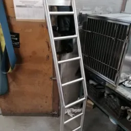 Metalowa drabina z okrągłych profili, stojąca w warsztacie, widoczne elementy wyposażenia i narzędzia.