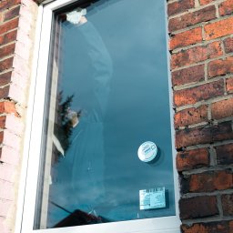 ODNOWA OKNA SPÓŁKA Z OGRANICZONĄ ODPOWIEDZIALNOŚCIĄ - Montaż okna w Dąbrowie Górniczej, widoczna ceglana ściana budynku i pracownik w odblasku szyby.