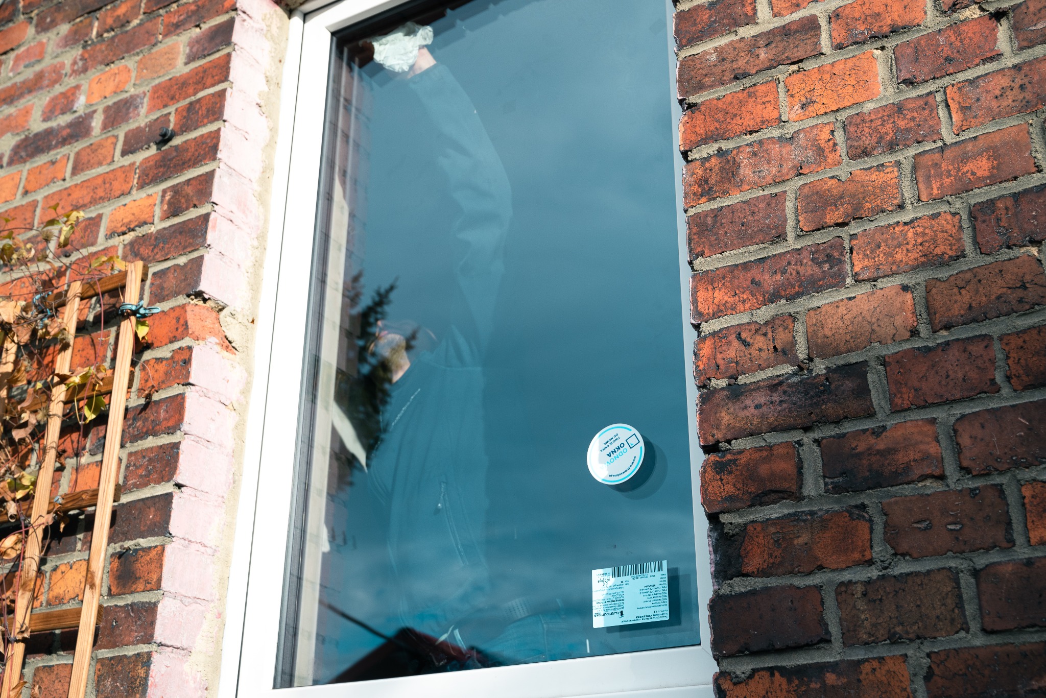 Montaż okna w Dąbrowie Górniczej, widoczna ceglana ściana budynku i pracownik w odblasku szyby.