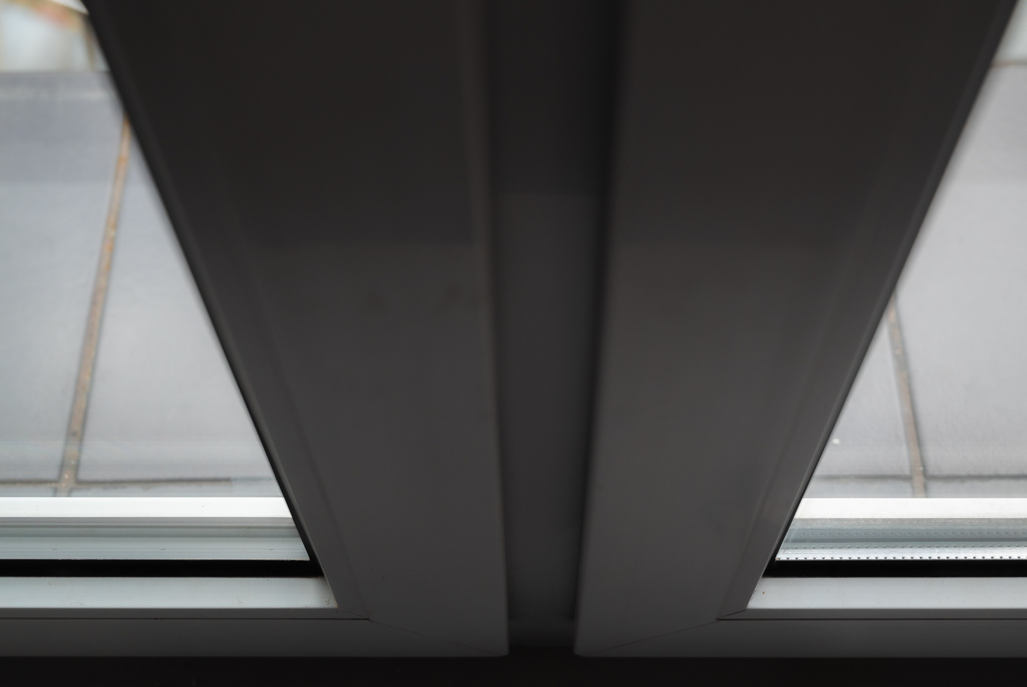 Widok z dołu na białą ramę okienną z szybą, widoczny fragment szarego parapetu zewnętrznego.