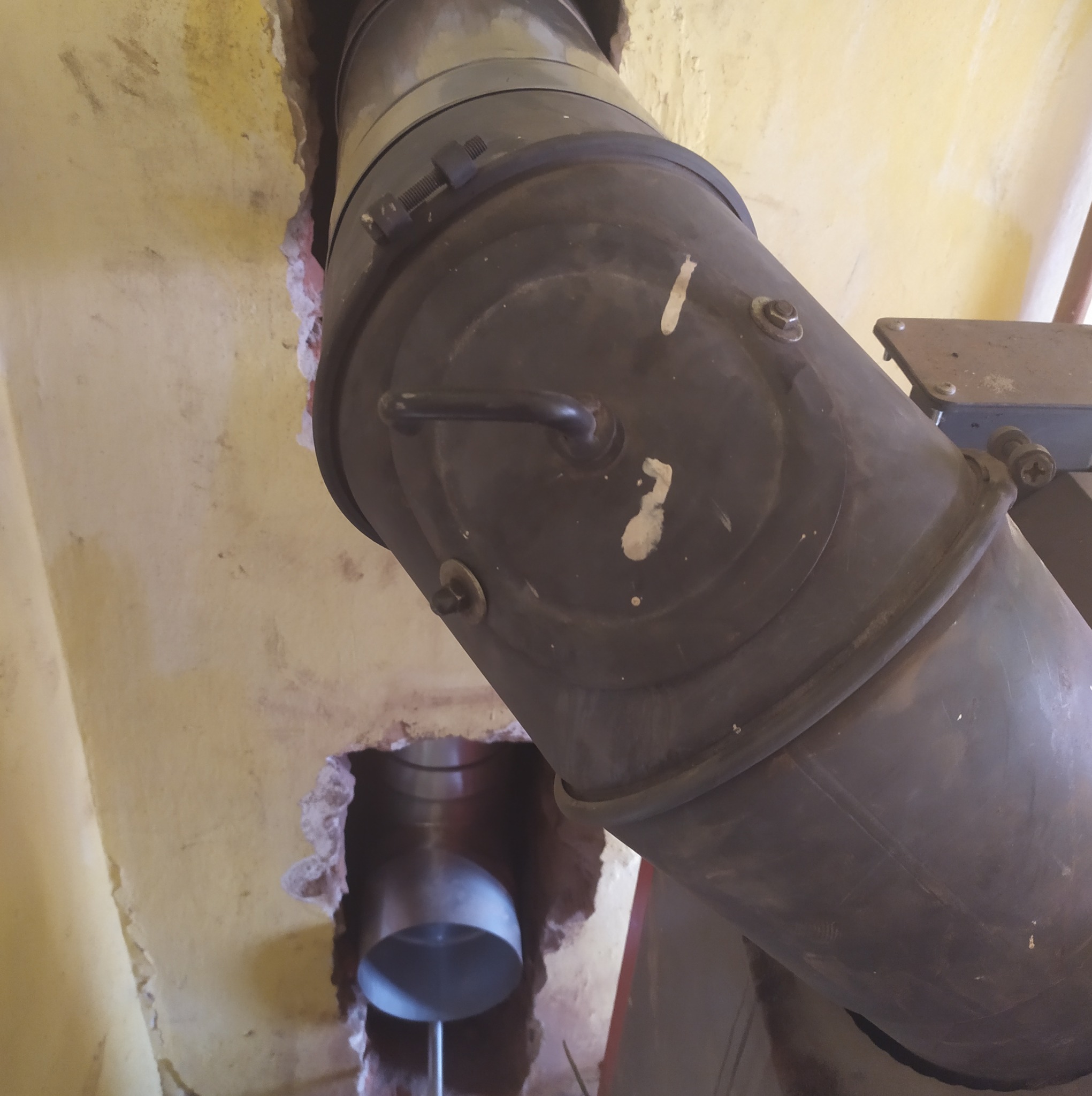 Metalowy przewód kominowy, połączony z otworem w ścianie, widoczne ślady po montażu.