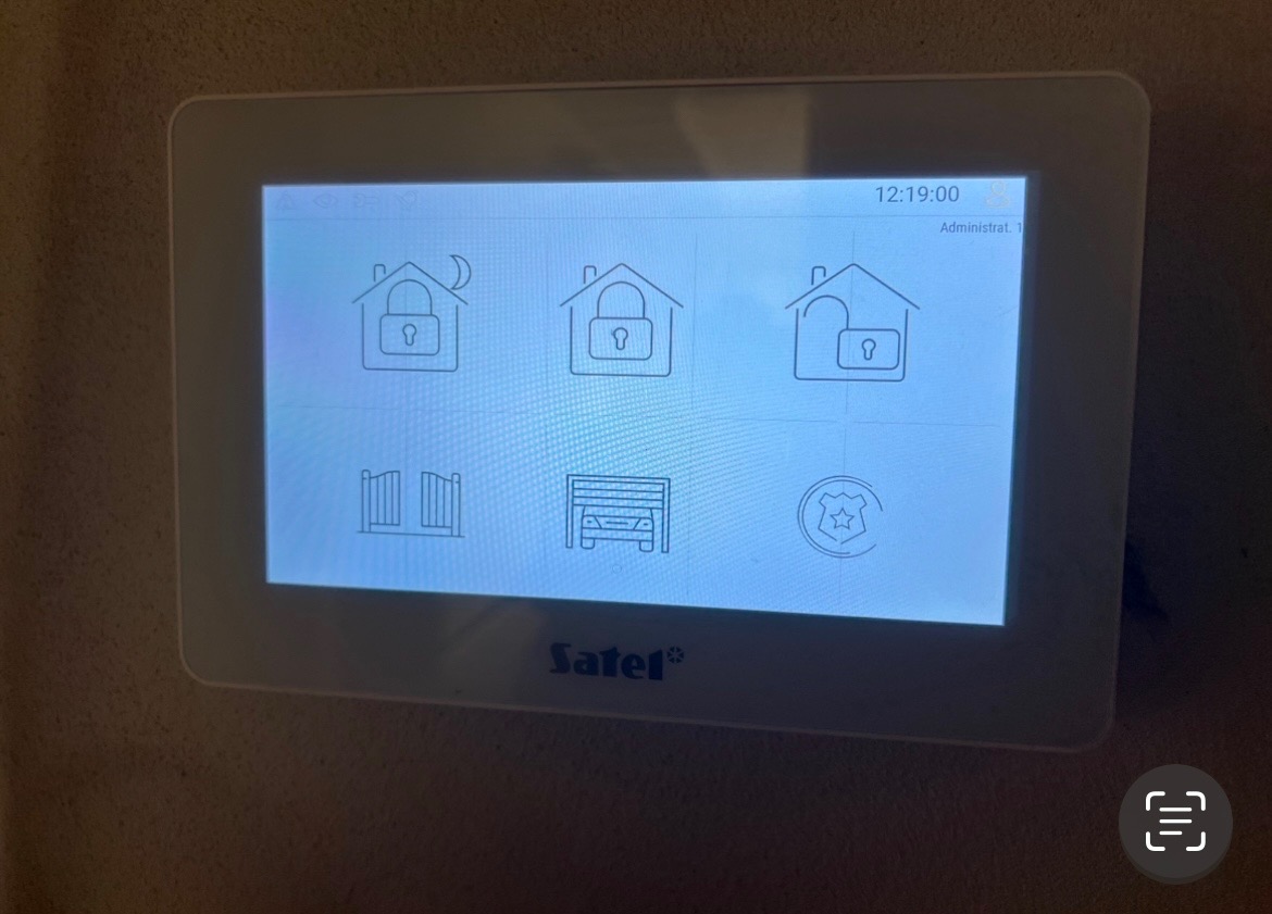 Ekran dotykowy systemu alarmowego z ikonami domu z kłódką, bramy i garażu, wyświetlający godzinę 12:19, z logo Satel u dołu.