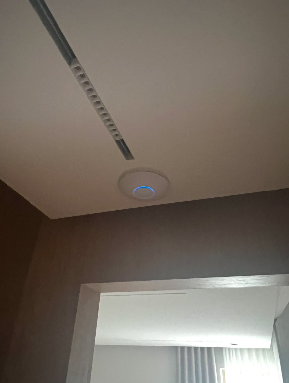 Zamontowany punkt dostępowy Wi-Fi z niebieską diodą na suficie w Radomiu, widoczny fragment listwy oświetleniowej i wejście do pokoju.