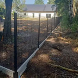 Nowoczesne ogrodzenie panelowe z podmur&oacute;wką betonową, widok z boku na tle domu i drzew.