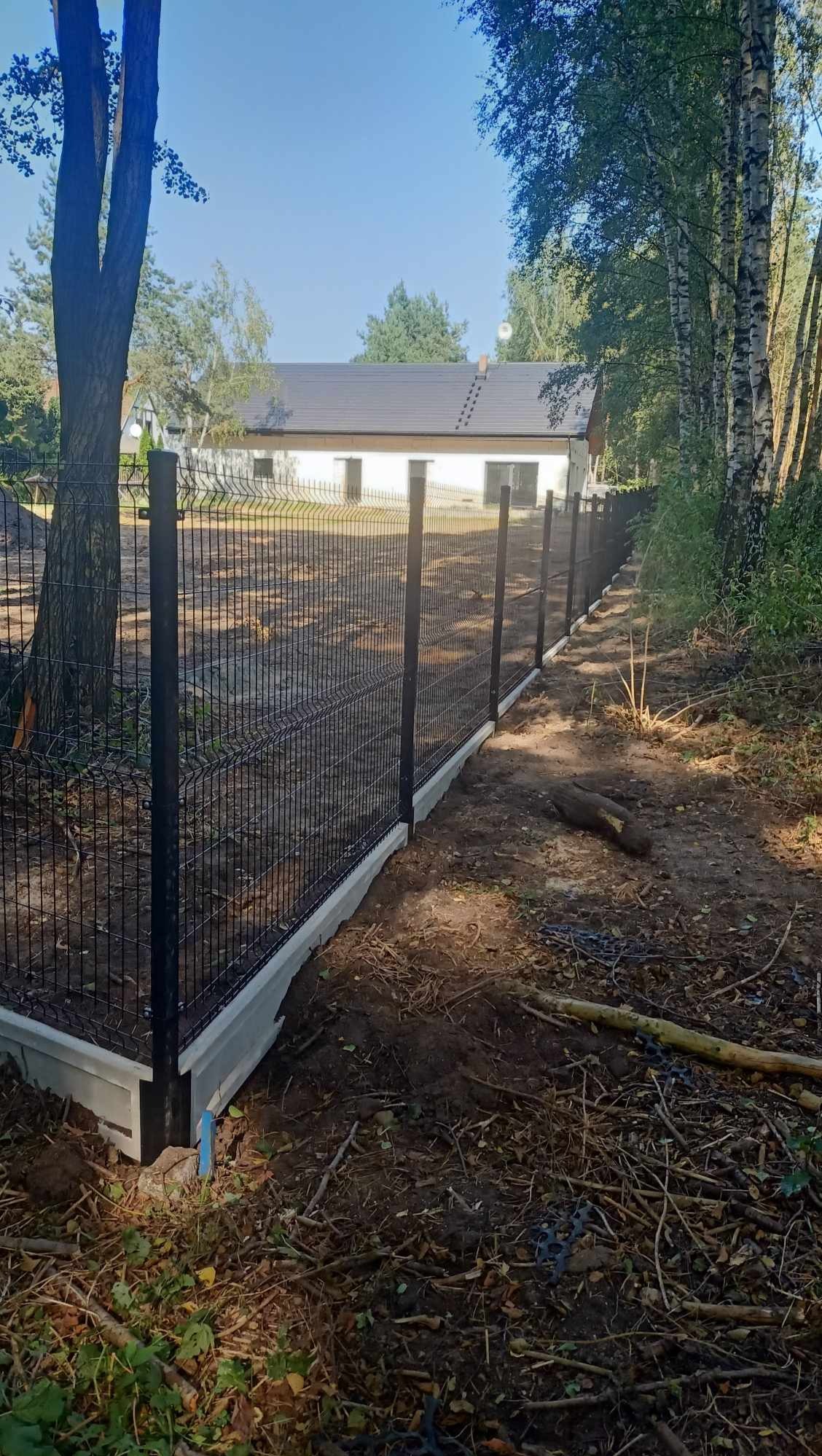 Nowoczesne ogrodzenie panelowe z podmurówką betonową, widok z boku na tle domu i drzew.