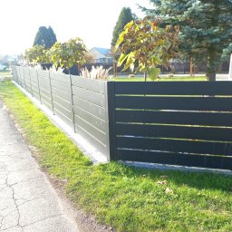 ARTUR MENŻYK - Nowoczesne, poziome przęsła ogrodzeniowe w kolorze grafitowym, oddzielające posesję od chodnika z popękanego asfaltu, z roślinami ozdobnymi posadzonymi wzdłuż ogrodzenia.