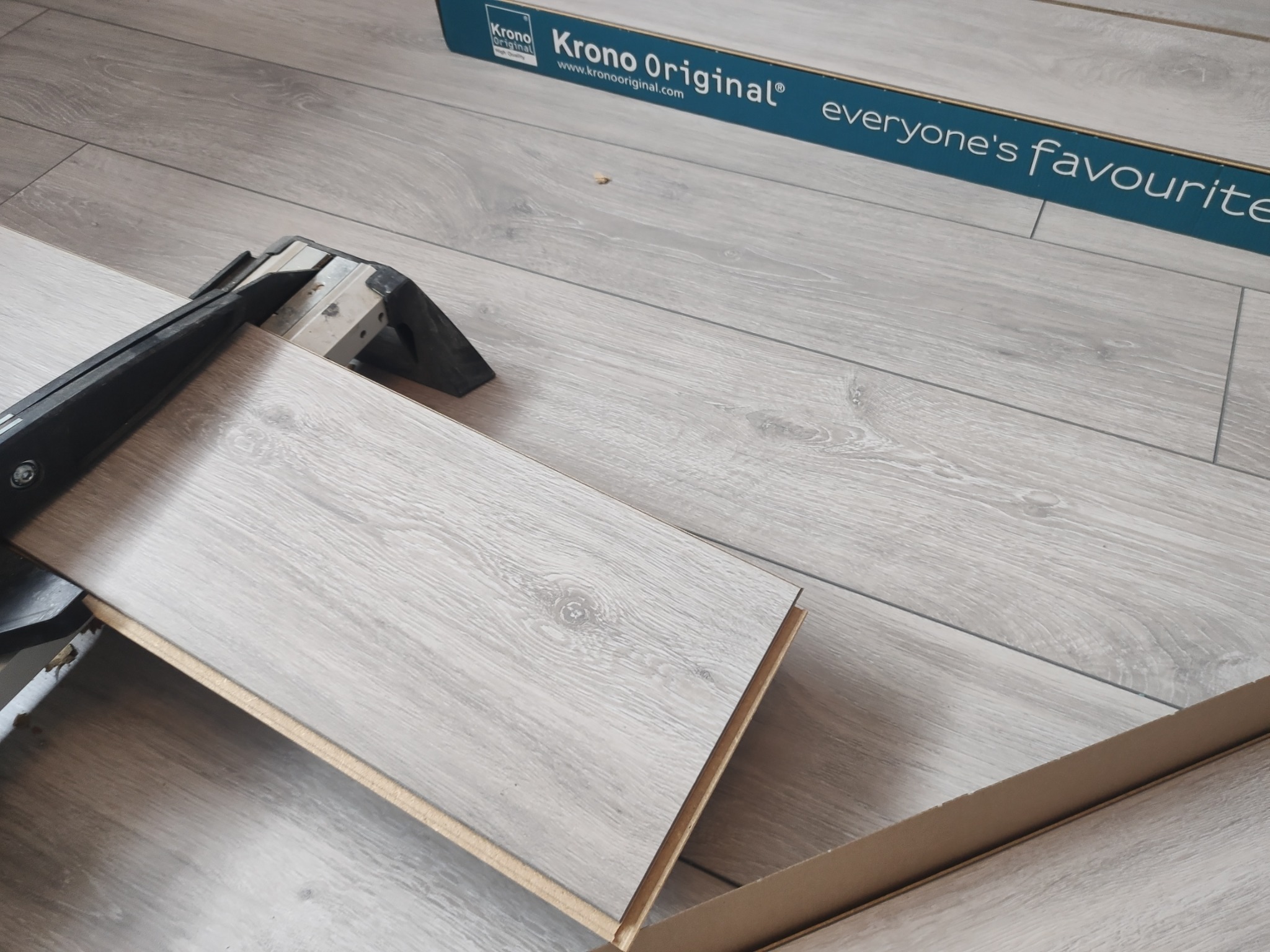 Przycięcie panela podłogowego Krono Original za pomocą gilotyny, widoczny fragment opakowania z hasłem 'everyone's favourite'.