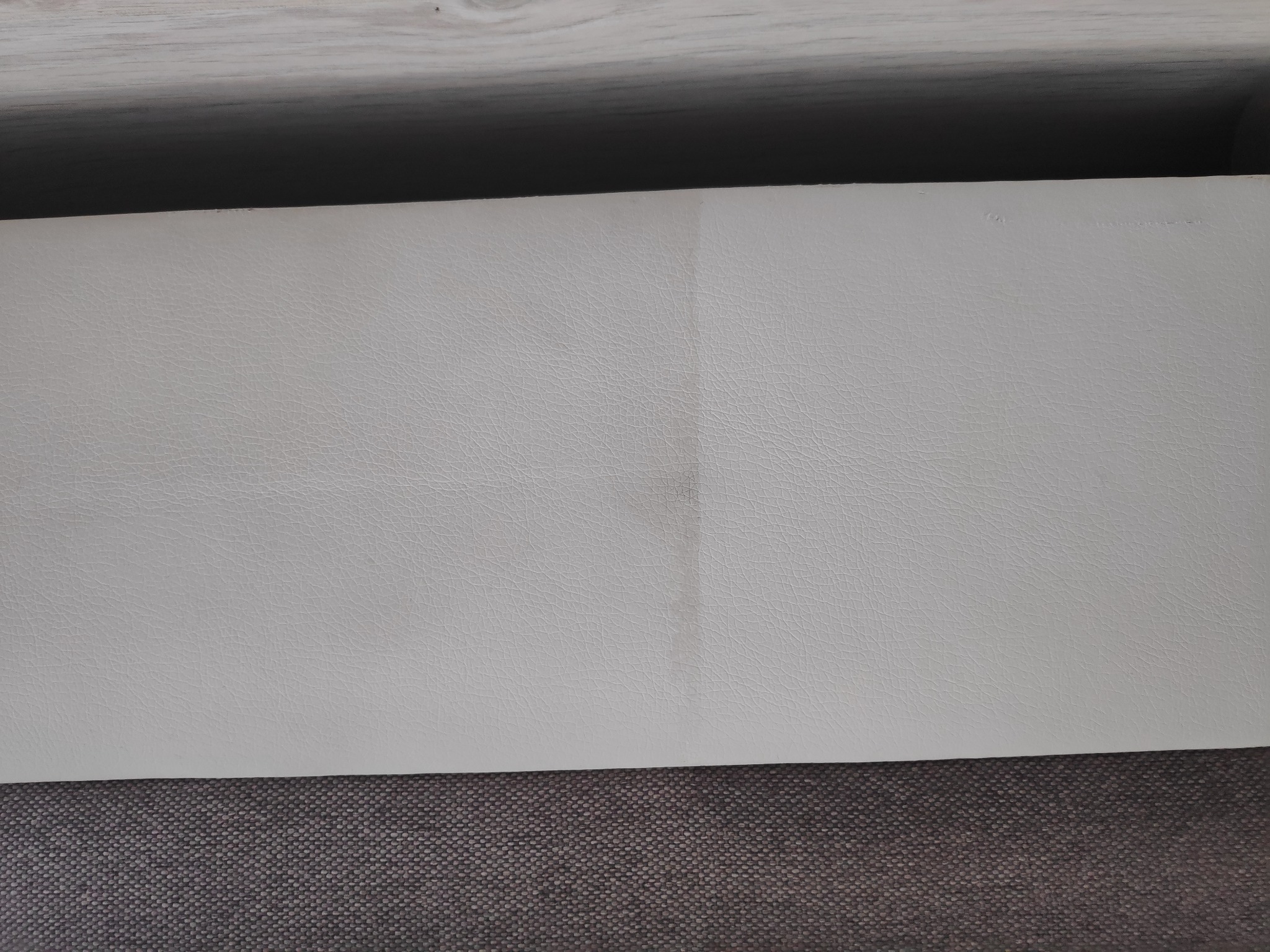 Fragment jasnej, skórzanej tapicerki meblowej z widocznym, delikatnym śladem po czyszczeniu, na tle szarej tkaniny.