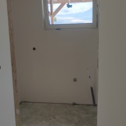 Serwis Remont - Przygotowane do malowania wnętrze z osadzonym oknem dachowym, widoczne ślady po szpachlowaniu, rurka instalacyjna przy ścianie, oraz wąż od odkurzacza i miarka na podłodze.