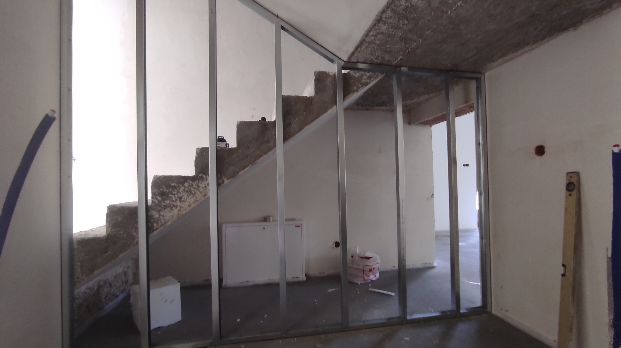 Stelaż z profili metalowych pod ścianę działową z płyty gipsowo-kartonowej na tle schodów w surowym stanie, widoczny poziomica i instalacja elektryczna.