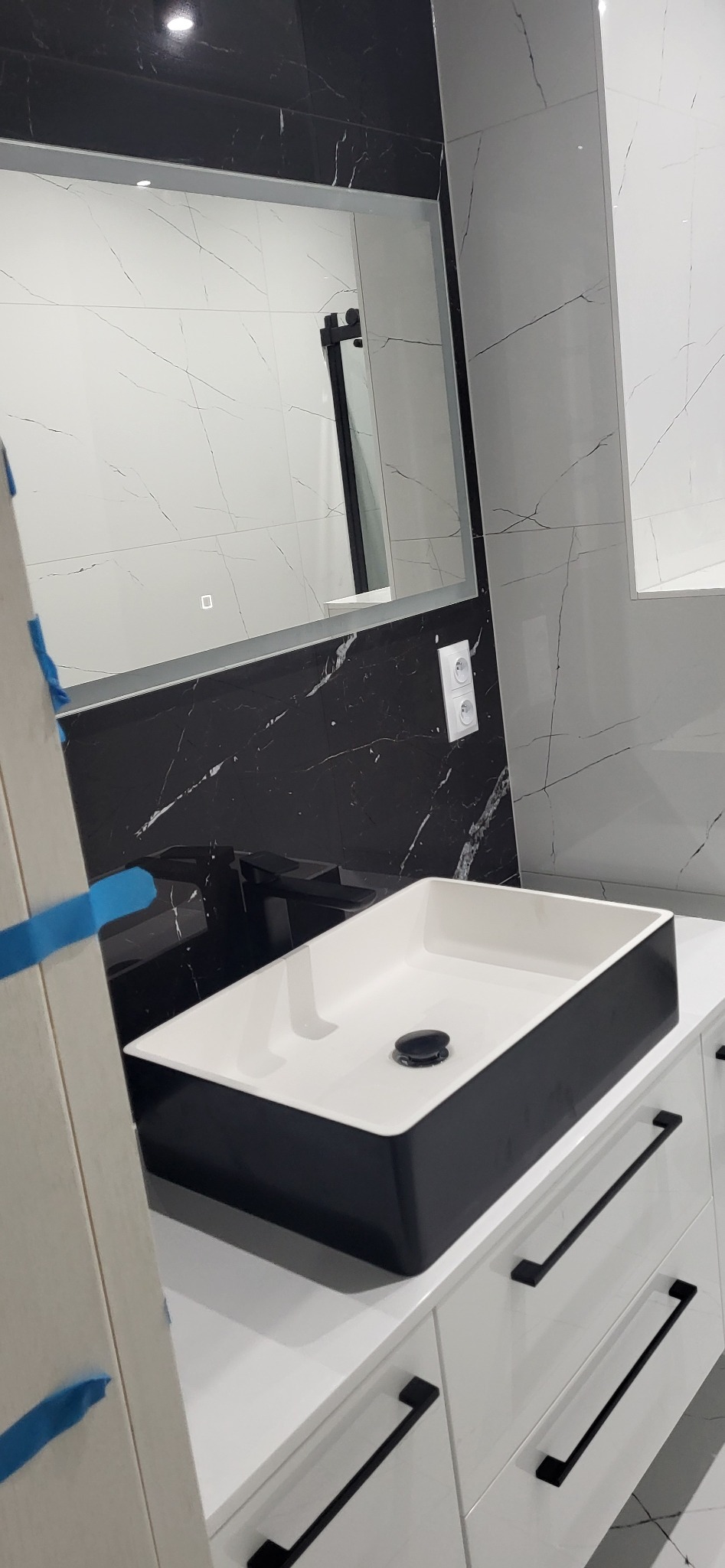 Nowoczesna łazienka z umywalką nablatową w czarno-białej kolorystyce, czarna armatura, marmurowe płytki i lustro z podświetleniem LED.