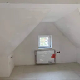 Poddasze w trakcie wykańczania: gładzie na skosach, okno w białej ramie, grzejnik w folii ochronnej, przygotowana podłoga.