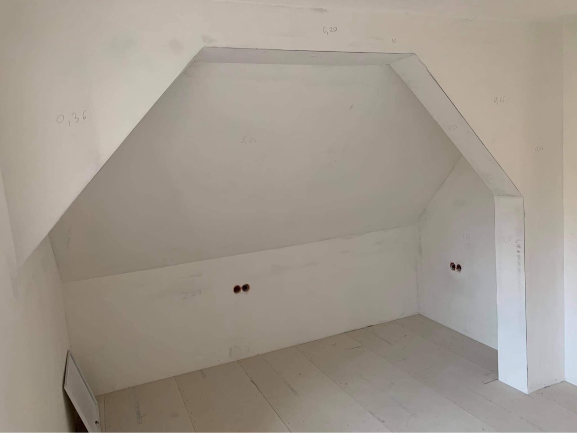 Poddasze w trakcie prac wykończeniowych, widoczne surowe ściany z naniesionymi pomiarami ołówkiem i przygotowane podłoże pod podłogę.