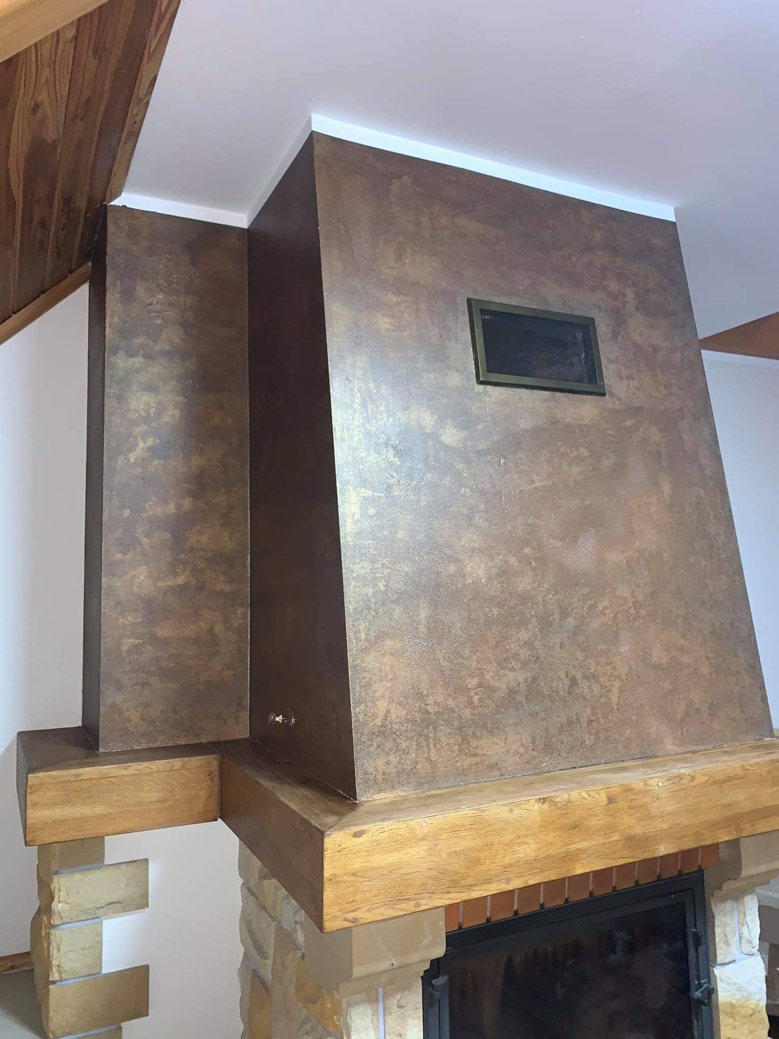 Ozdobna ściana kominkowa z efektem rdzy, drewniane belki w stylu rustykalnym i kamienna obudowa paleniska.