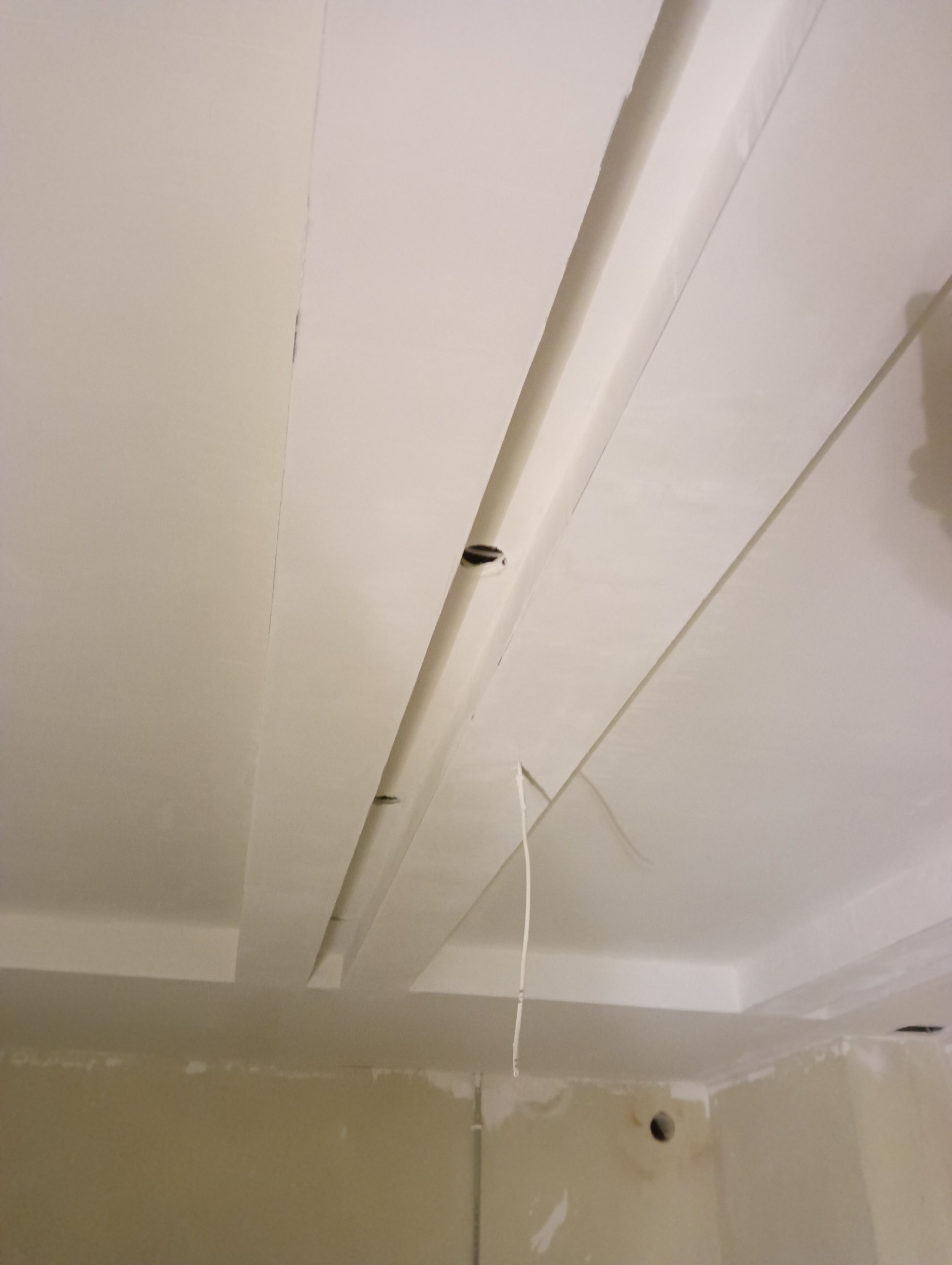 Sufit podwieszany z elementami dekoracyjnymi w trakcie montażu, widoczne przewody i niedokończone wykończenie ścian.