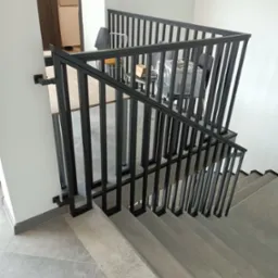 Schody betonowe z czarną, metalową balustradą o pionowych szczeblach, widok z góry na klatkę schodową w nowoczesnym budynku.