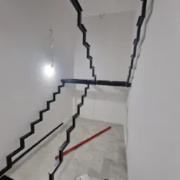 Wnętrze w trakcie montażu metalowej konstrukcji schodów z czarnych profili, widoczny poziomica i resztki pianki montażowej na podłodze.