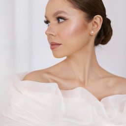 BIELEC ART - fotografia - Portret Panny Młodej z profilu, elegancka fryzura upięta w kok, perłowy kolczyk, delikatny makijaż, biała suknia z falbanami.