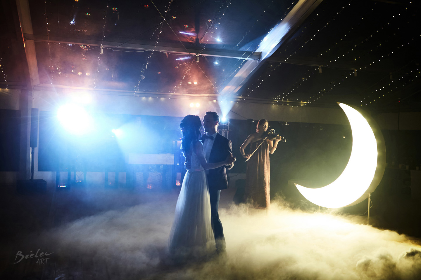 Para młoda w tańcu, przygrywa skrzypaczka, dekoracja w kształcie księżyca, ciężki dym na parkiecie, oświetlenie sceniczne.