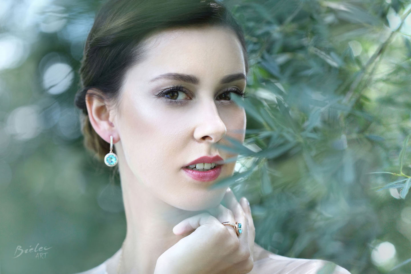 Portret panny młodej z biżuterią z akwamarynem, subtelny makijaż, liście w tle, profesjonalna sesja plenerowa.