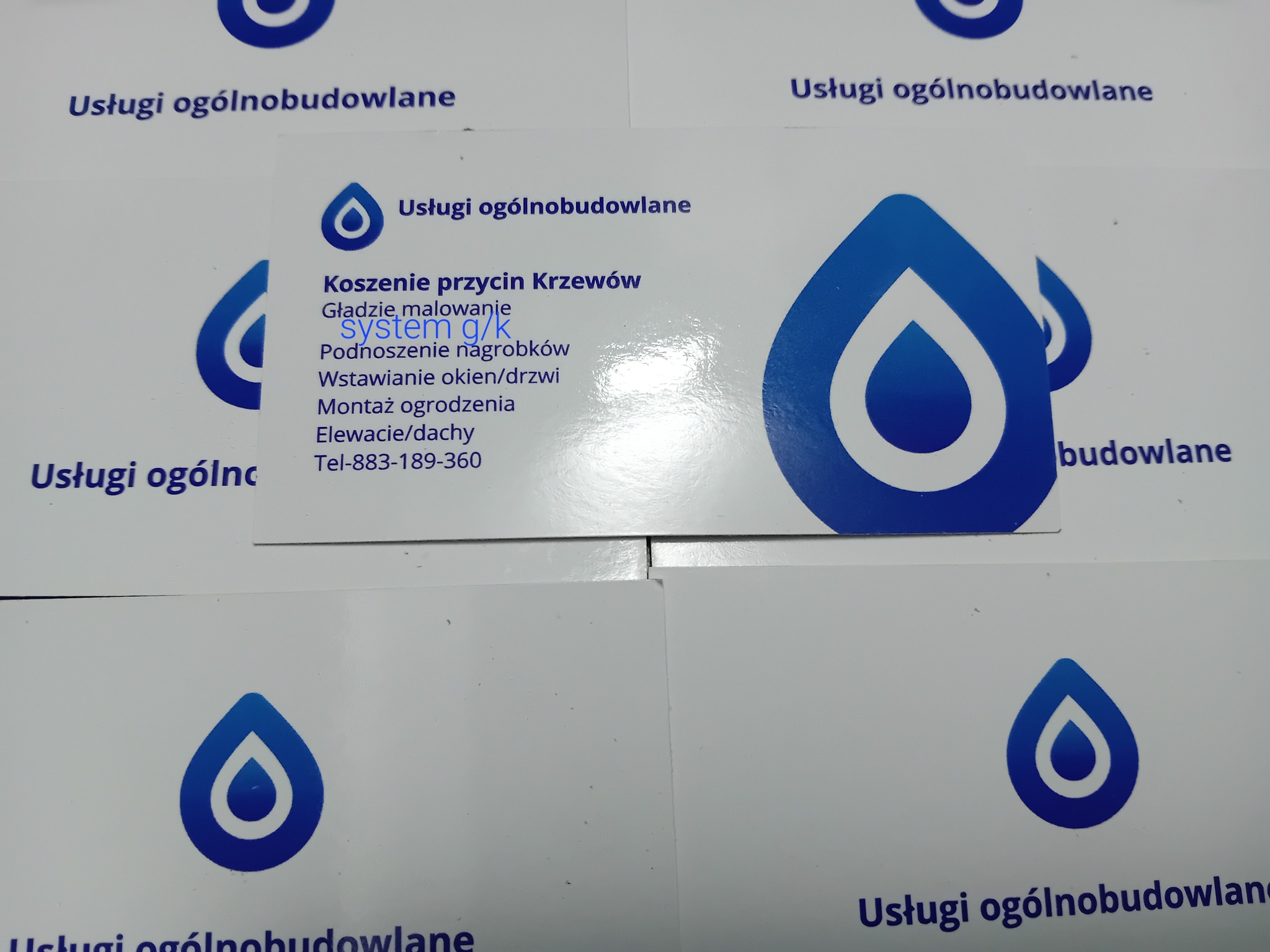 Wizytówki firmy budowlanej z niebieskim logo kropli wody i spisem usług: koszenie krzewów, gładzie, malowanie, podnoszenie nagrobków, wstawianie okien/drzwi, montaż ogrodzenia, elewacje/dachy...