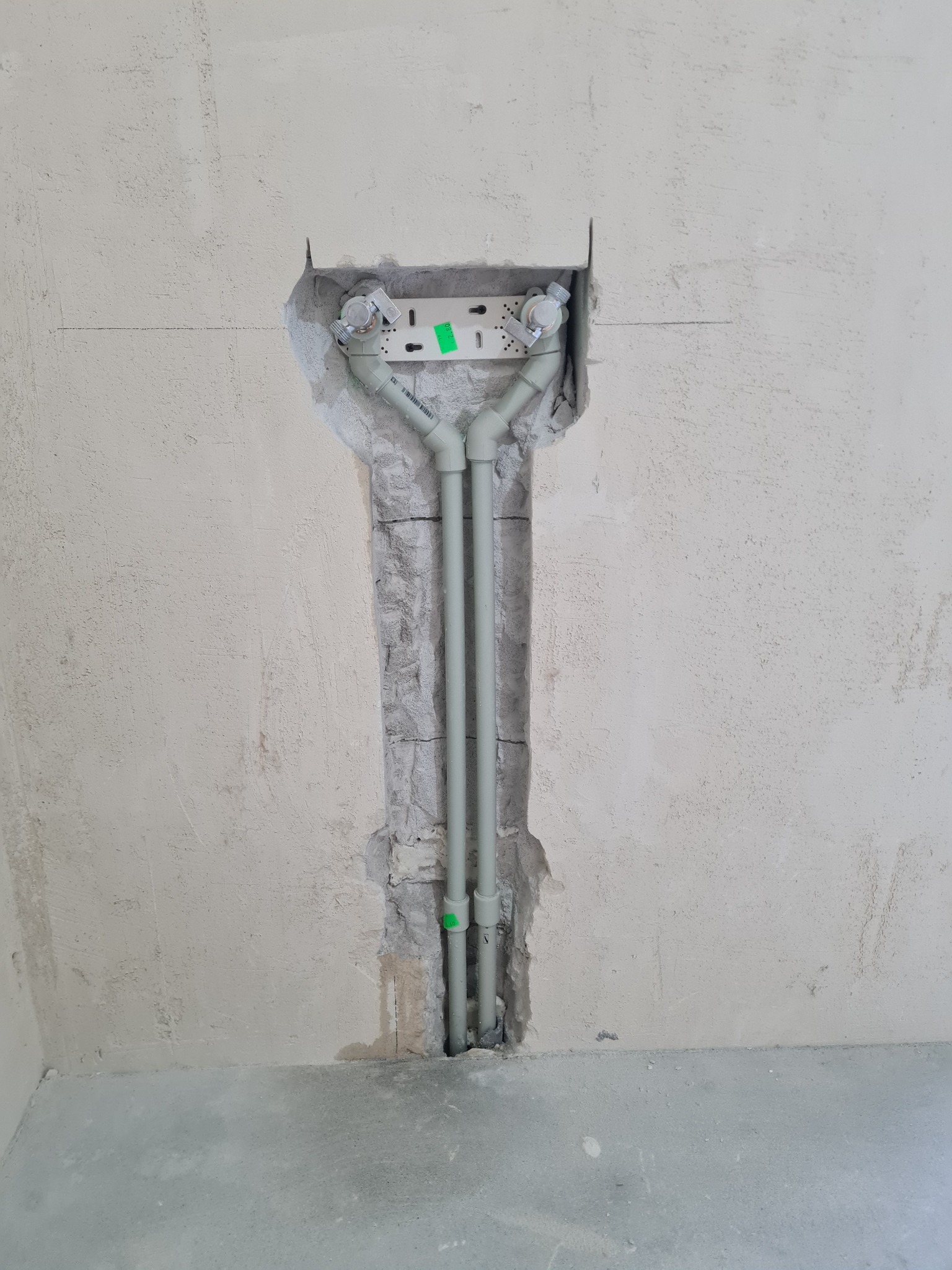 Instalacja wodna z rur PP-R w bruździe ściany, widoczne złącza i uchwyty montażowe, ściana w stanie surowym przed wykończeniem, podłoga betonowa.