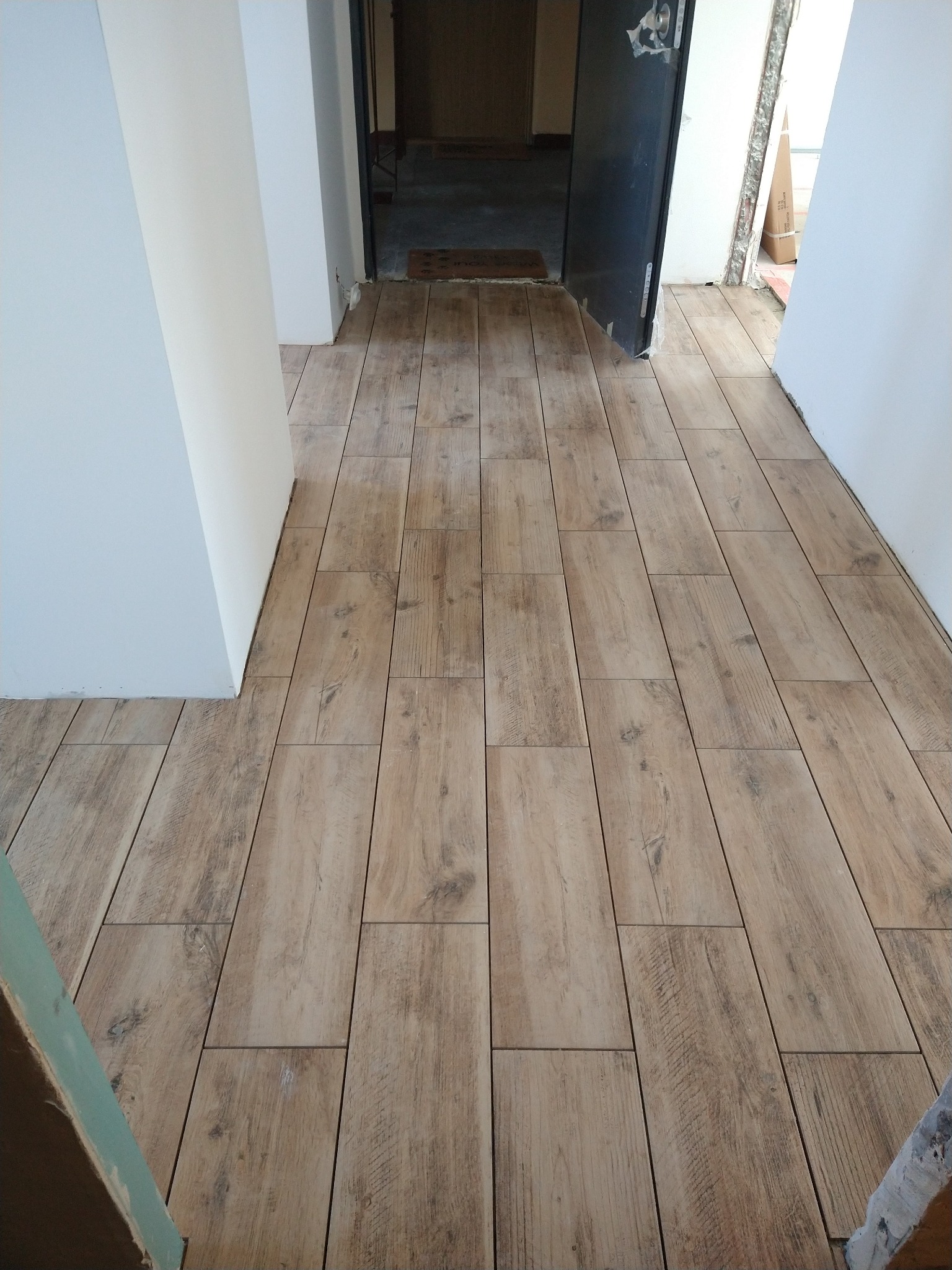 Ułożona podłoga z płytek imitujących drewno w korytarzu, widok z góry, fuga w kolorze zbliżonym do koloru płytek, białe ściany.