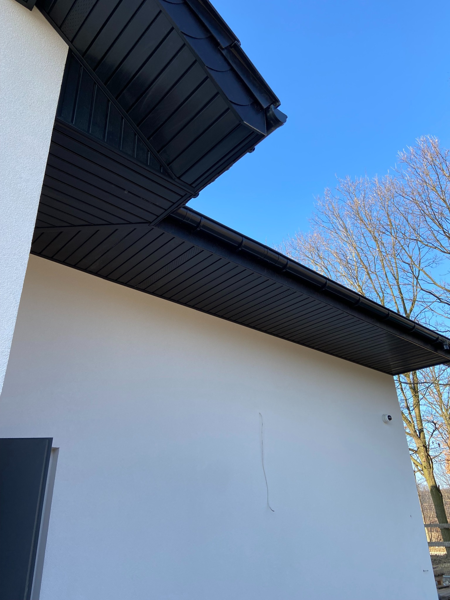 Elewacja budynku w Chwostku z widocznym fragmentem ocieplenia podbitki dachowej w kolorze czarnym i kamerą monitoringu na ścianie.